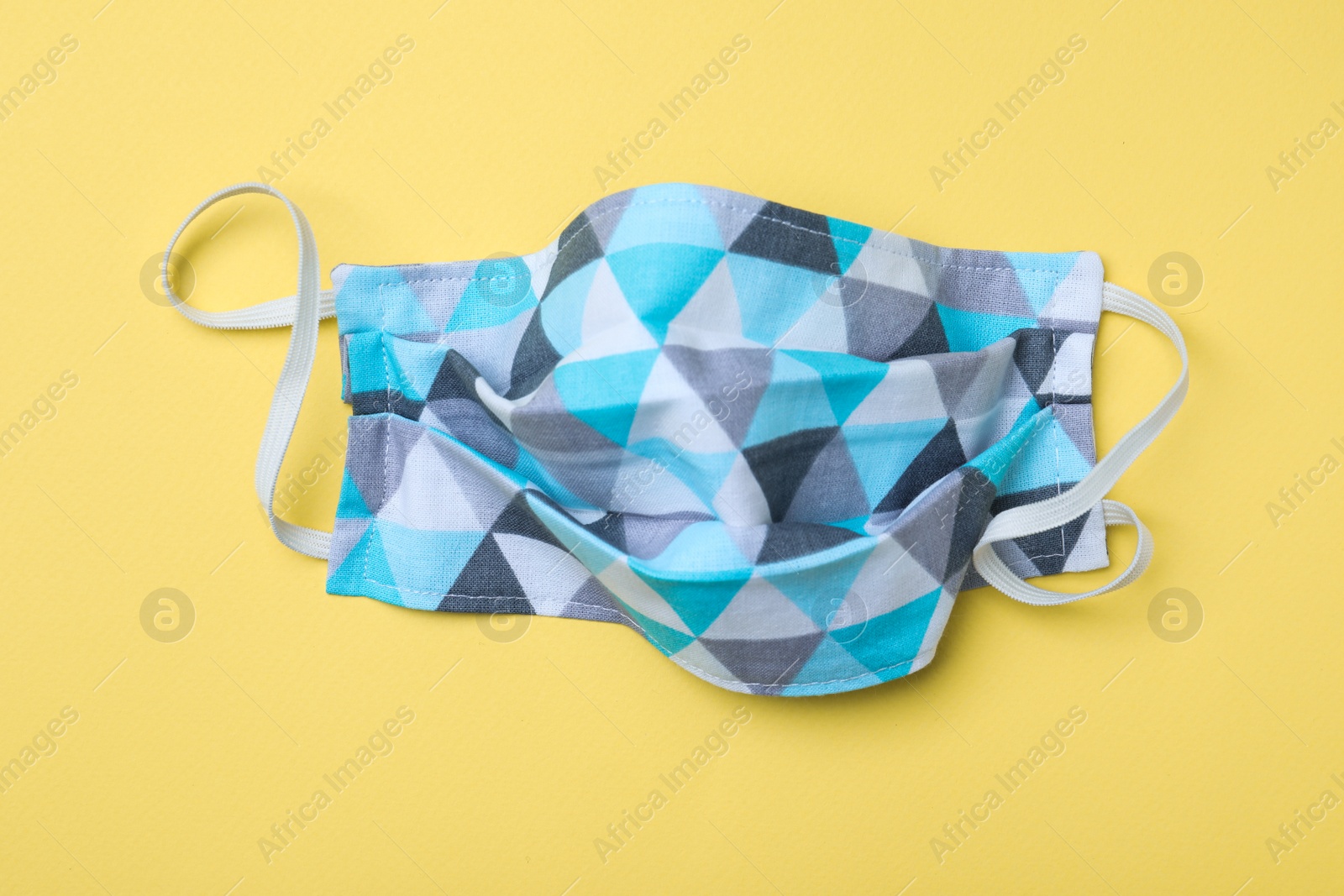 Photo of Homemade protective mask on yellow background, top view. Sewing idea