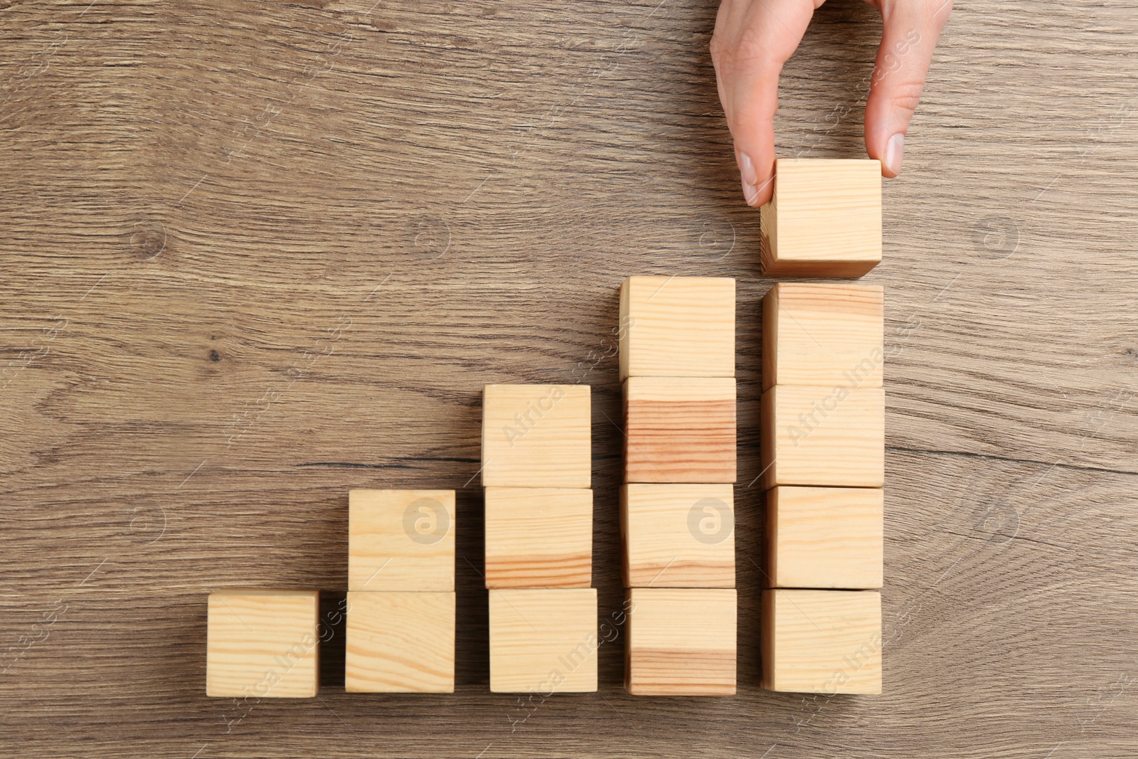 Photo of Woman building steps with wooden cubes on table, top view. Career promotion concept