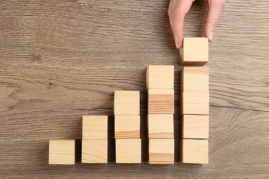 Woman building steps with wooden cubes on table, top view. Career promotion concept