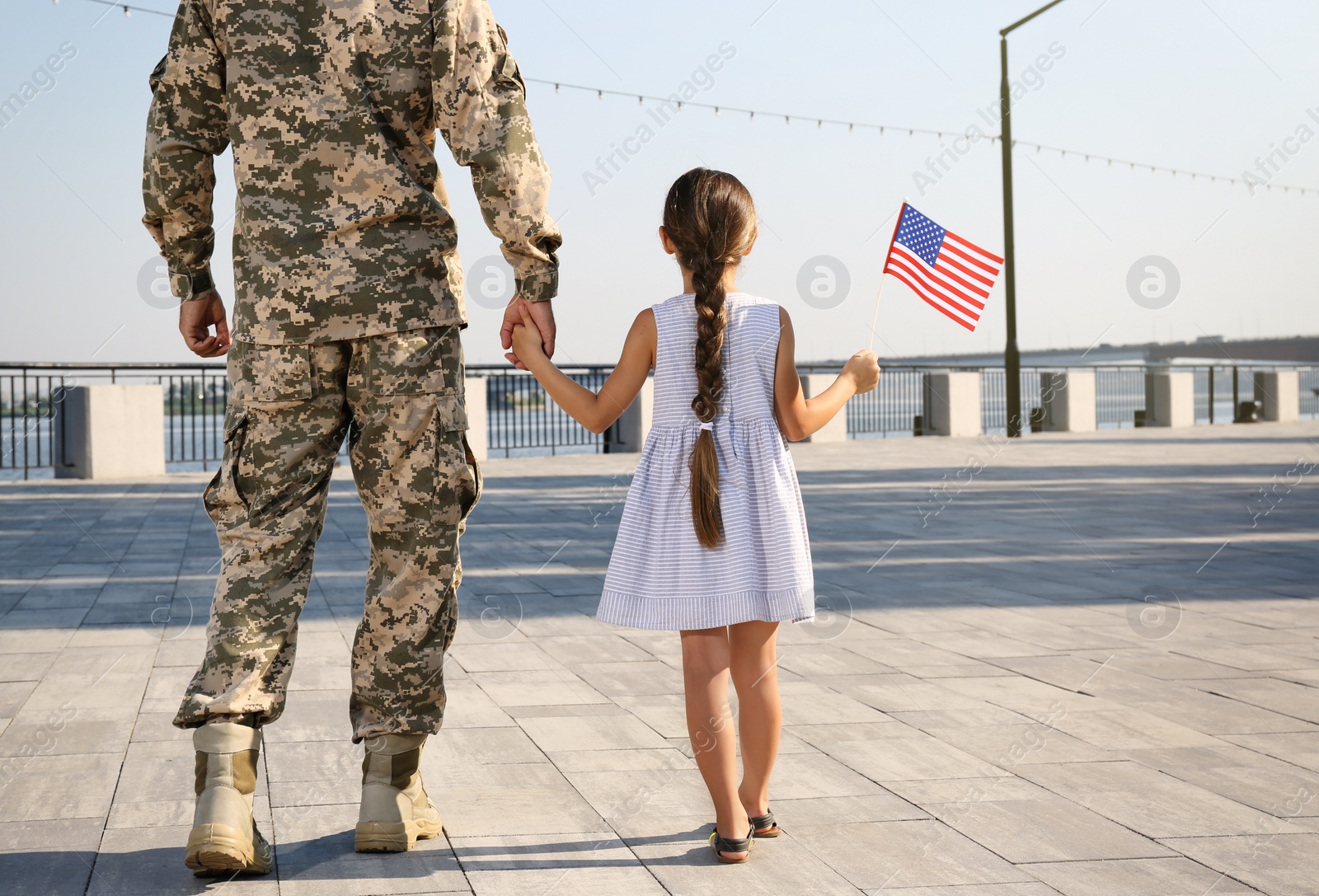 Photo of Soldier and his little daughter with American flag outdoors, back view. Veterans Day in USA