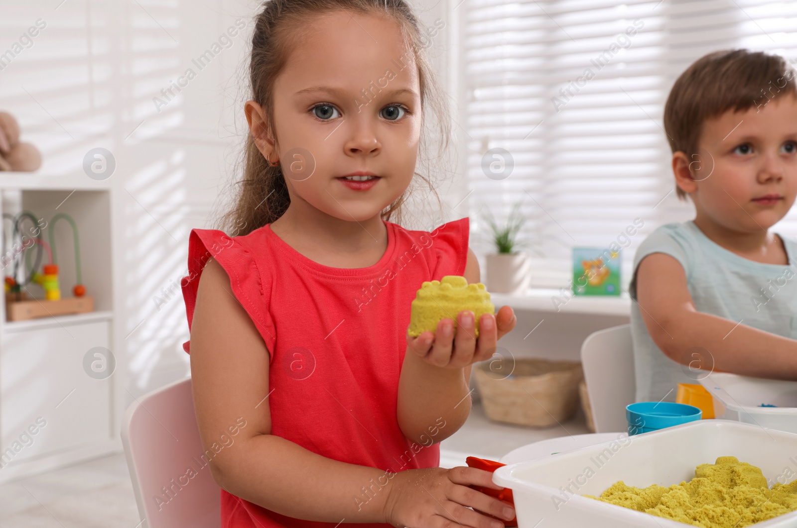 Photo of Cute little children playing with bright kinetic sand at table in room