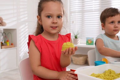 Photo of Cute little children playing with bright kinetic sand at table in room