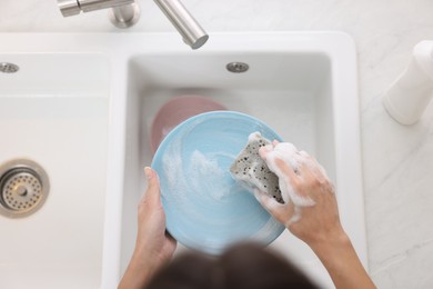 Photo of Woman washing plate above sink in modern kitchen, top view