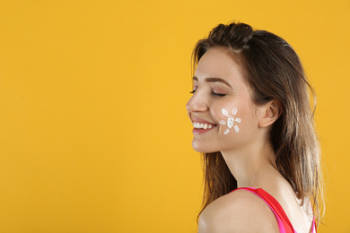 Young woman with sun protection cream on face against yellow background. Space for text