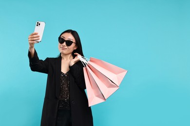 Photo of Beautiful woman with shopping bags taking selfie on light blue background. Space for text