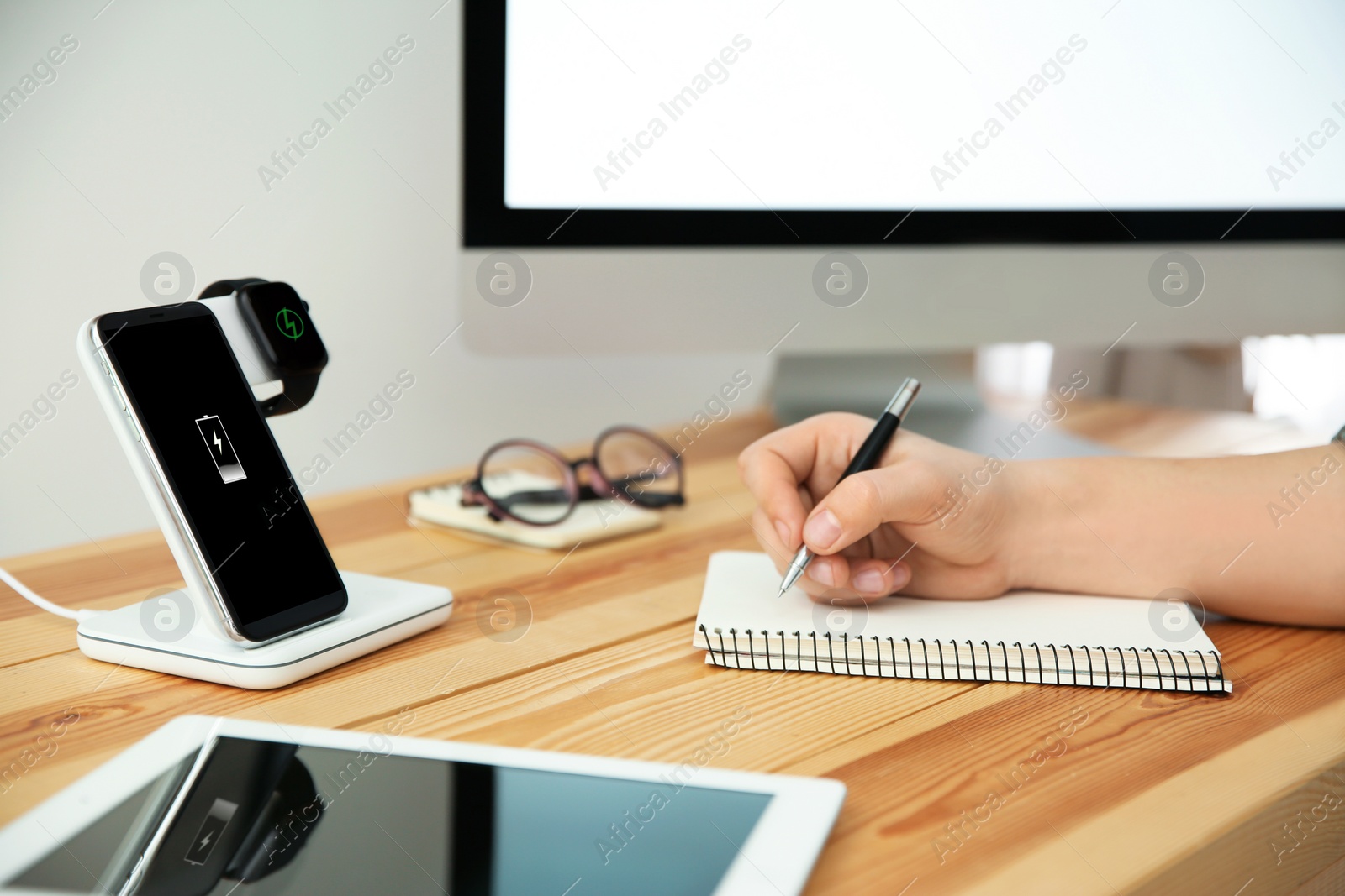 Photo of Man working at table while his mobile phone and smartwatch charging with wireless device