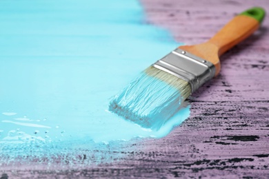 Photo of Brush with blue paint on pink wooden background, space for text