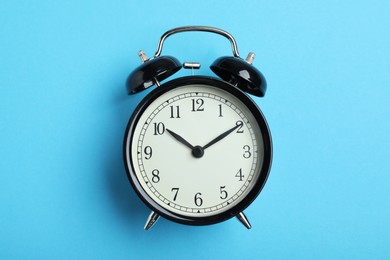 Alarm clock on light blue background, top view. School time