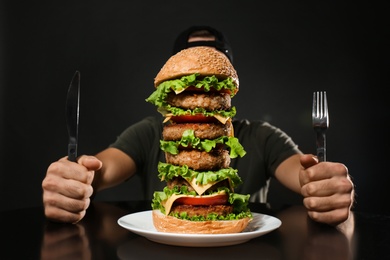 Photo of Man with cutlery eating huge burger on black background