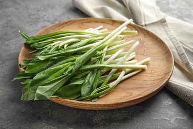 Photo of Wooden plate with wild garlic or ramson on grey table