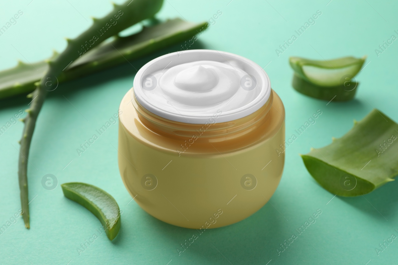 Photo of Jar of natural cream and aloe leaves on green background, closeup