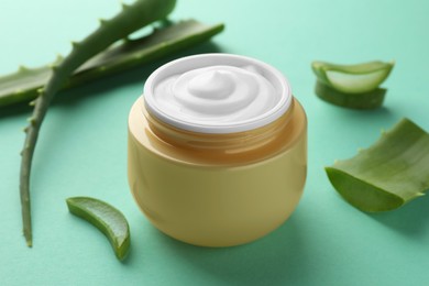Photo of Jarnatural cream and aloe leaves on green background, closeup
