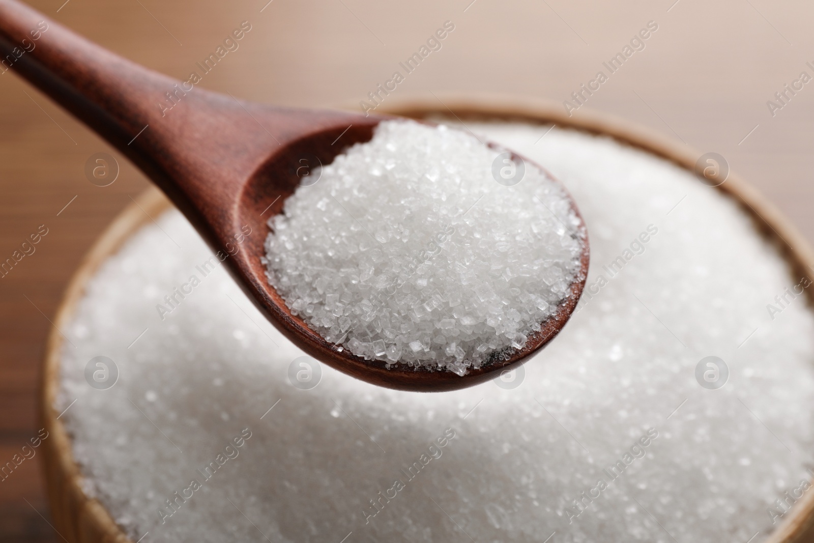 Photo of Spoon with granulated sugar over bowl, closeup