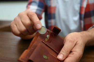 Senior man putting coin into purse at table, closeup