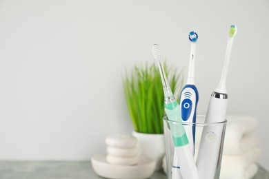 Photo of Electric toothbrushes in glass near white wall, closeup. Space for text