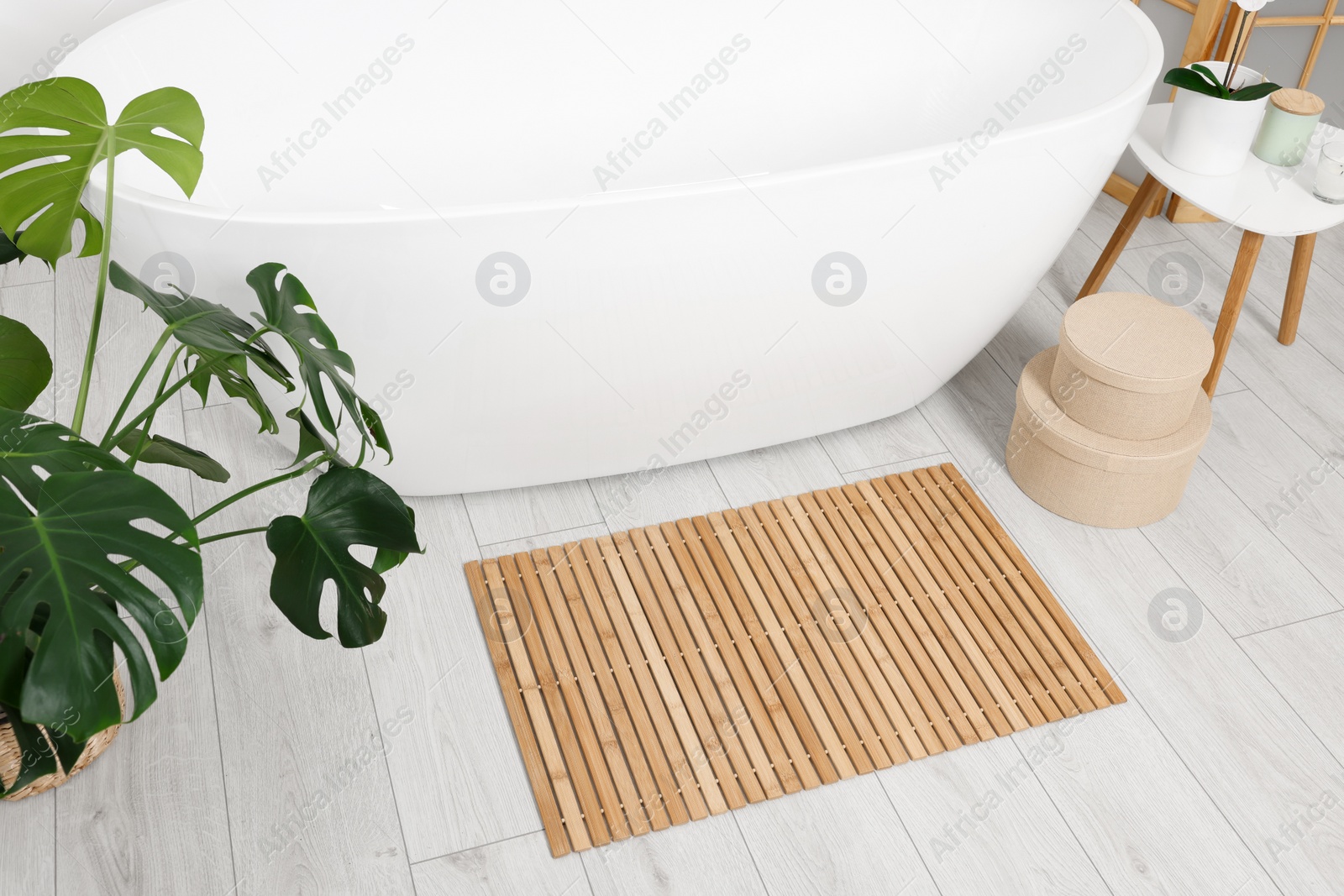 Photo of Stylish bathroom interior with bath tub, houseplant and bamboo mat