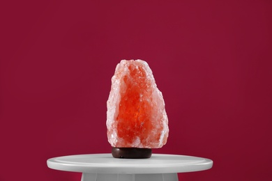 Himalayan salt lamp on white table against dark pink background