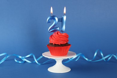 Photo of Delicious cupcake with number shaped candles on blue background. Coming of age party - 21th birthday