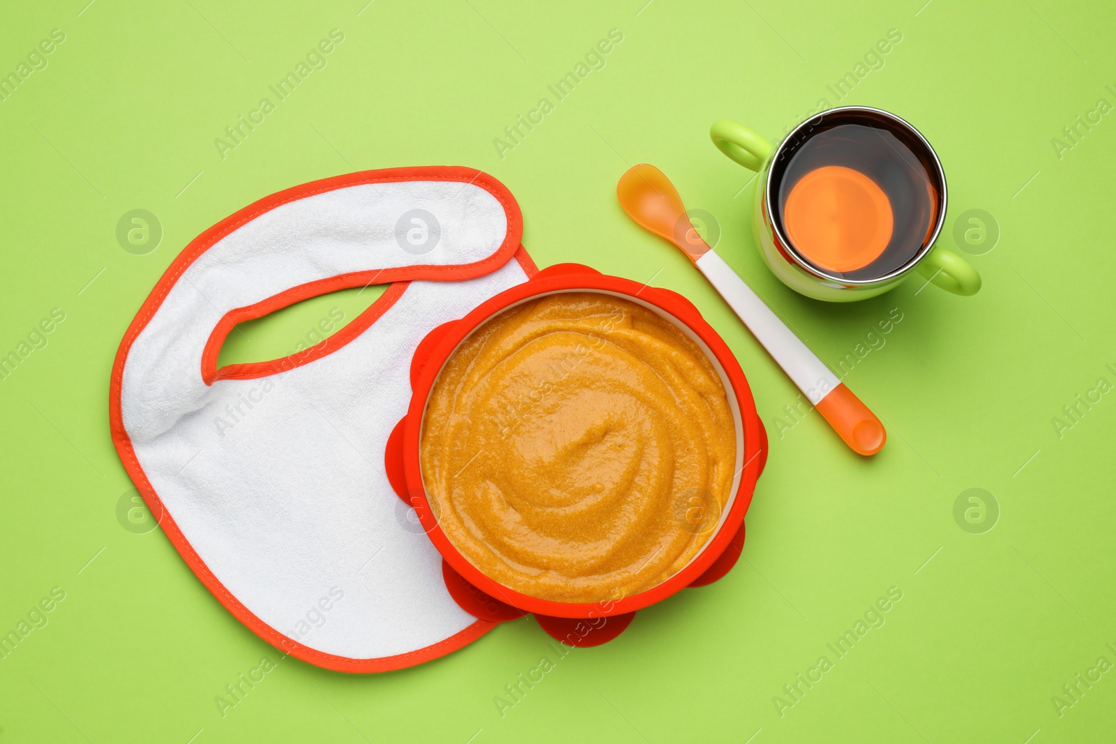 Photo of Baby bib and plastic dishware with healthy food on light green background, flat lay