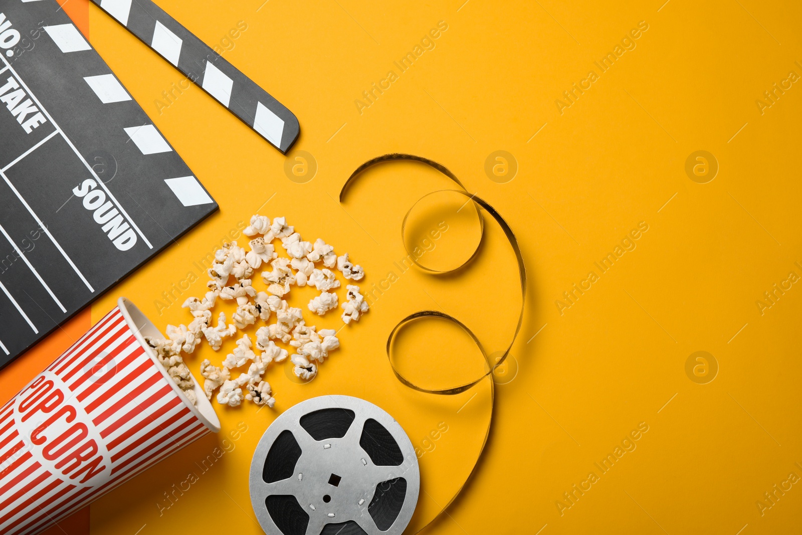 Photo of Clapperboard, popcorn and film reel on orange background, flat lay. Space for text