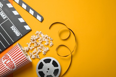 Photo of Clapperboard, popcorn and film reel on orange background, flat lay. Space for text