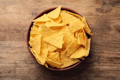Bowl of tasty tortilla chips (nachos) on wooden table, top view