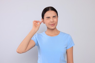 Young woman cleaning ear with cotton swab on light grey background