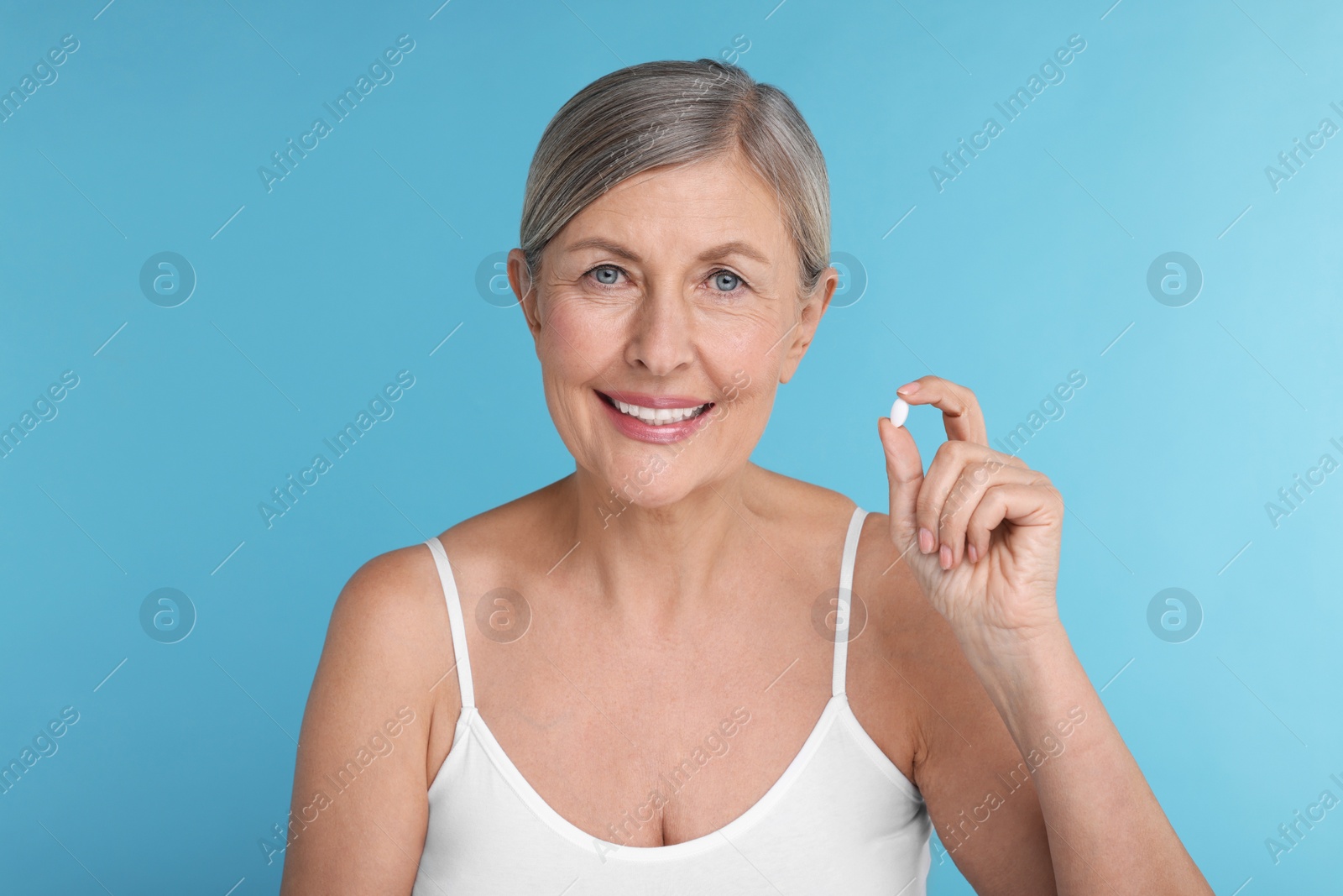 Photo of Beautiful woman with vitamin pill on light blue background