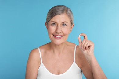 Beautiful woman with vitamin pill on light blue background