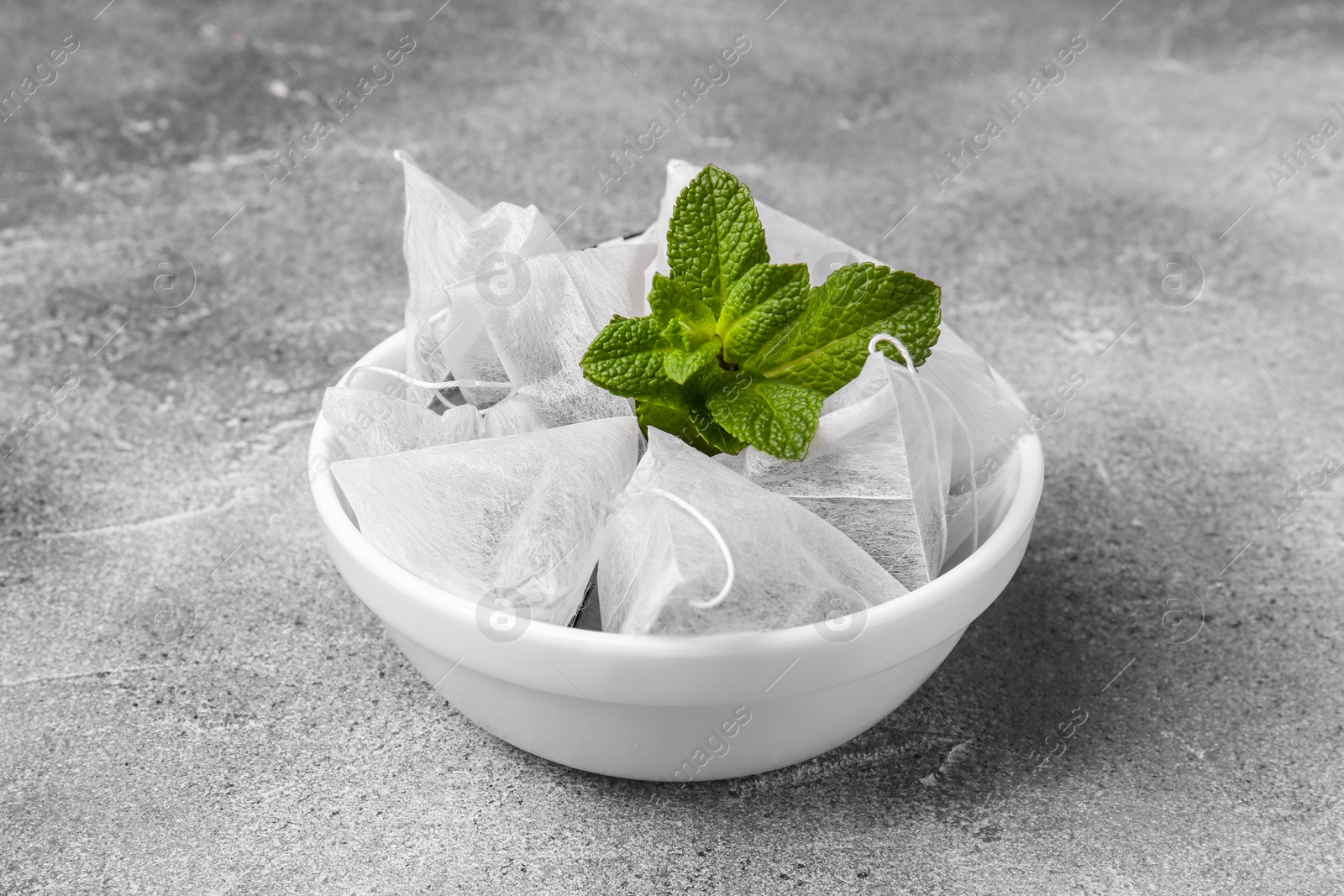 Photo of Tea bags and mint on light grey table, closeup