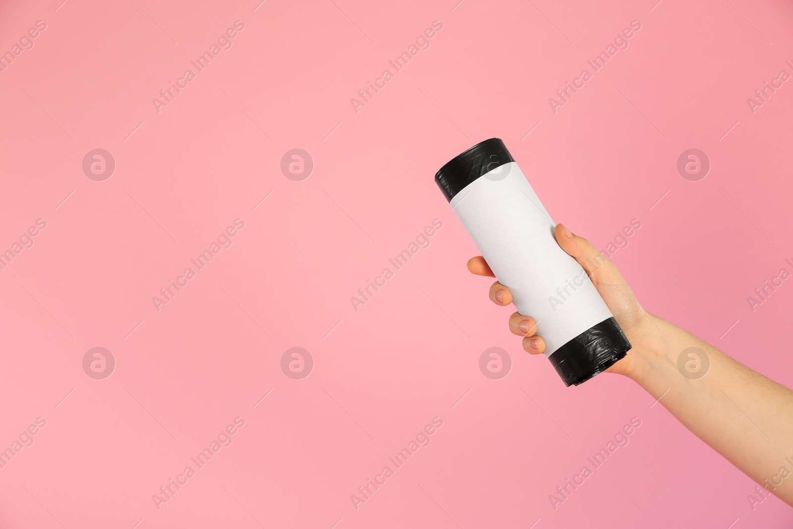 Photo of Woman holding roll of black garbage bags on pink background, closeup. Space for text