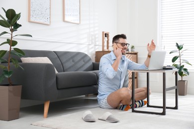 Businessman in shirt and underwear talking on phone during video call at home