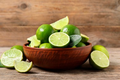 Photo of Tasty ripe limes in bowl on wooden table, closeup