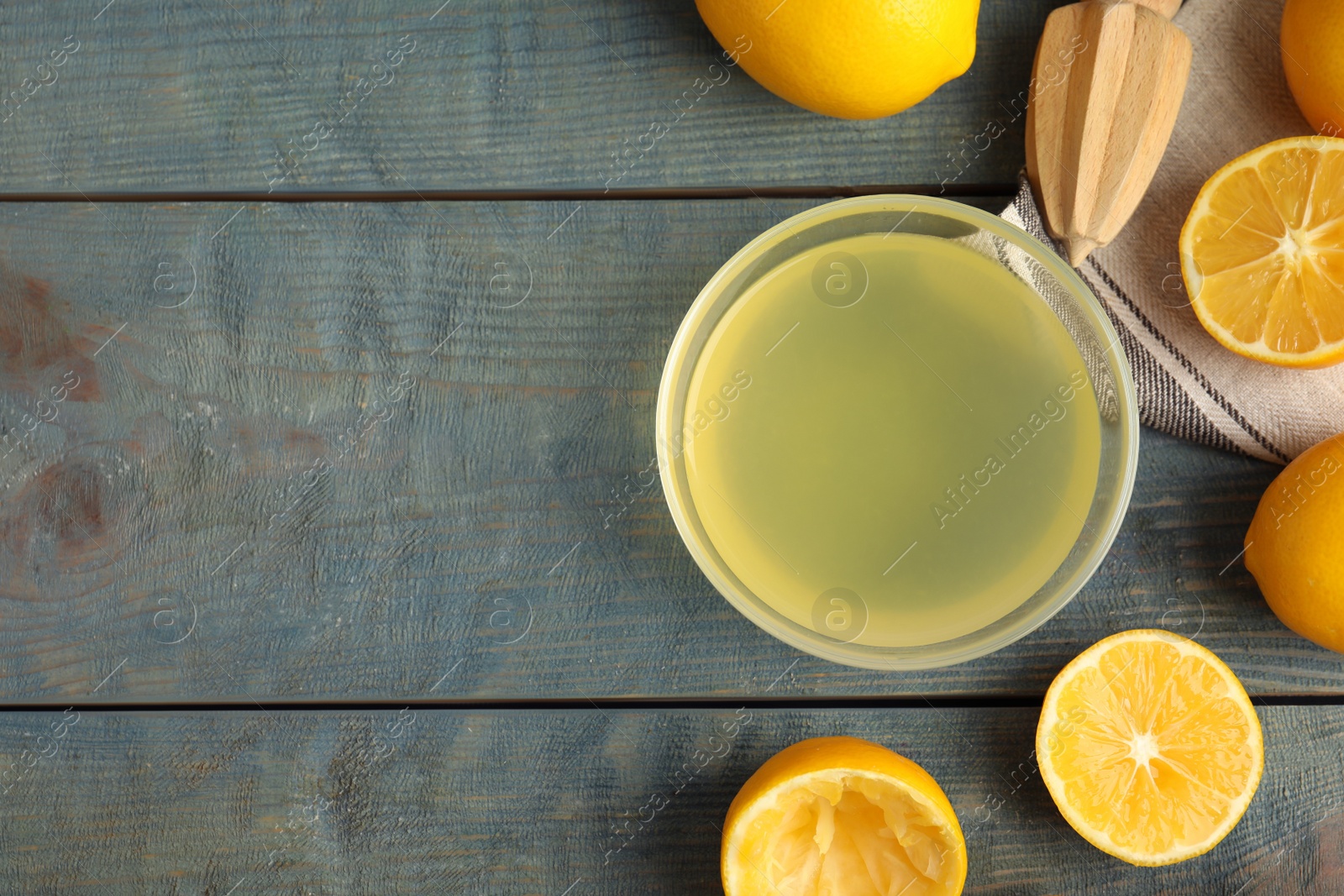 Photo of Freshly squeezed lemon juice on blue wooden table, flat lay. Space for text