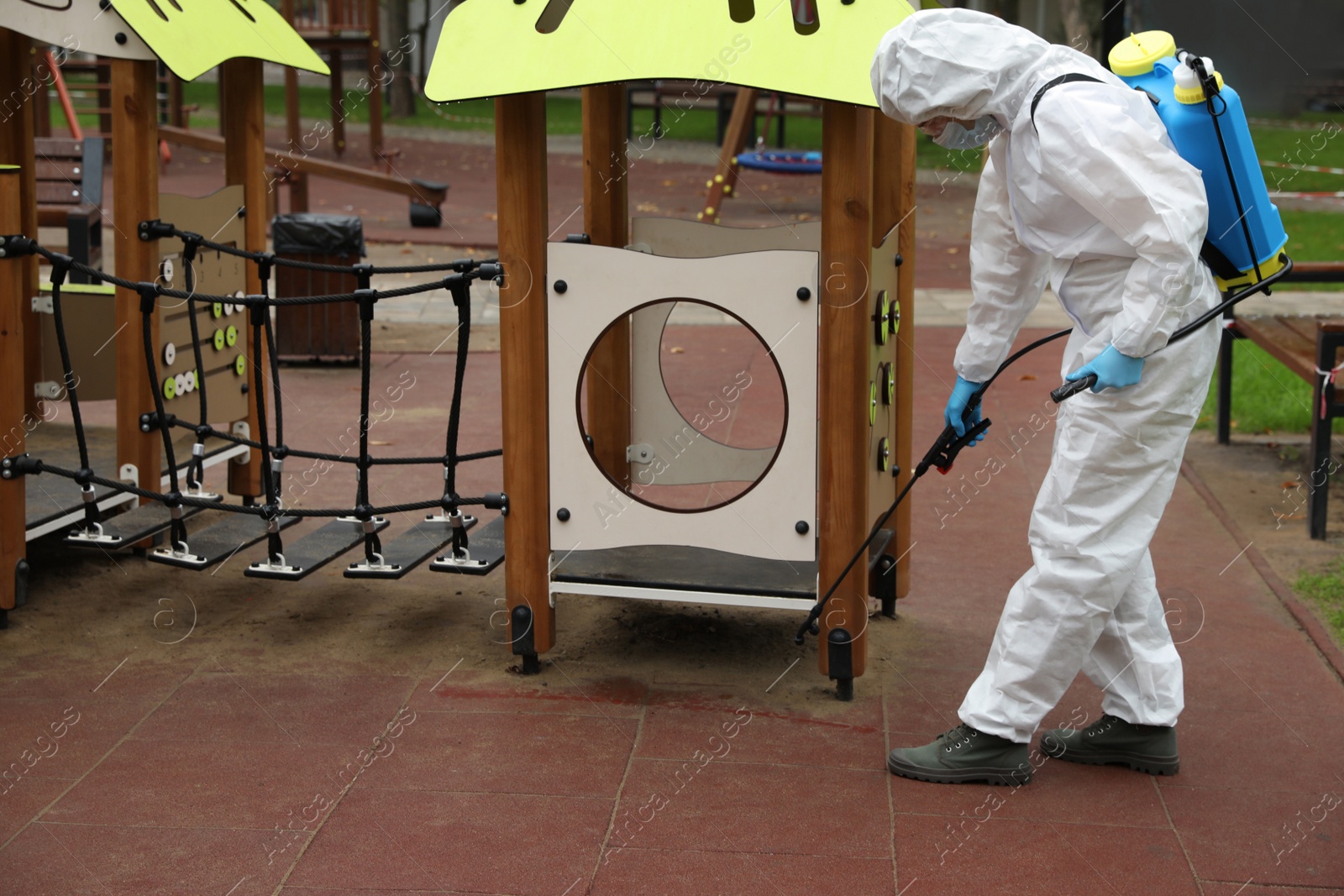 Photo of Woman wearing chemical protective suit with disinfectant sprayer on playground. Preventive measure during coronavirus pandemic