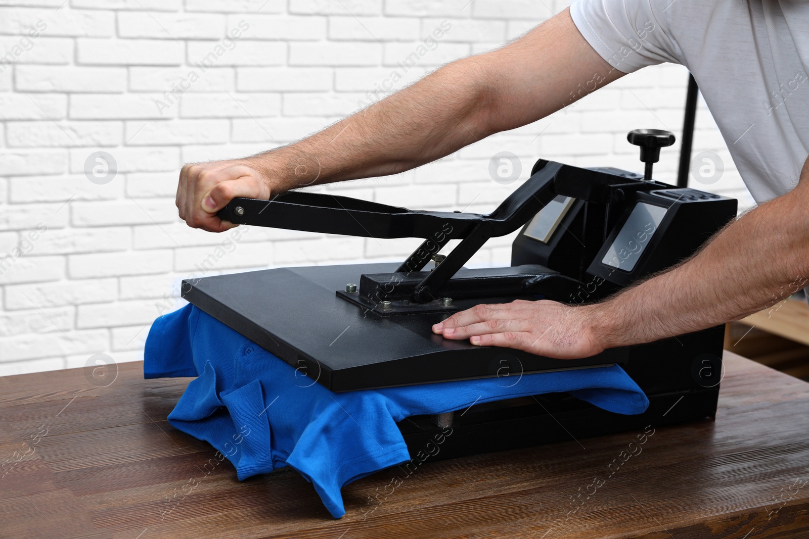 Photo of Man using heat press machine at table near white brick wall, closeup