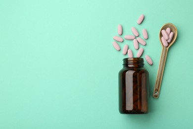 Photo of Vitamin pills, bottle and spoon on mint color background, flat lay. Space for text