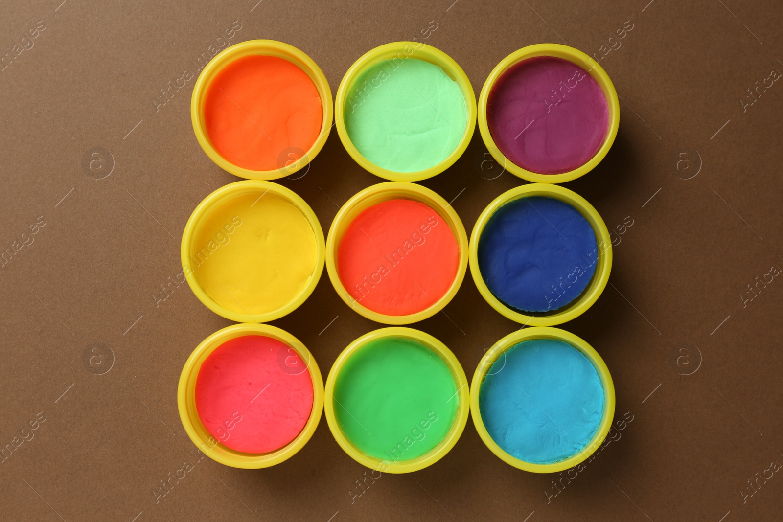 Photo of Plastic containers with colorful play dough on brown background, flat lay
