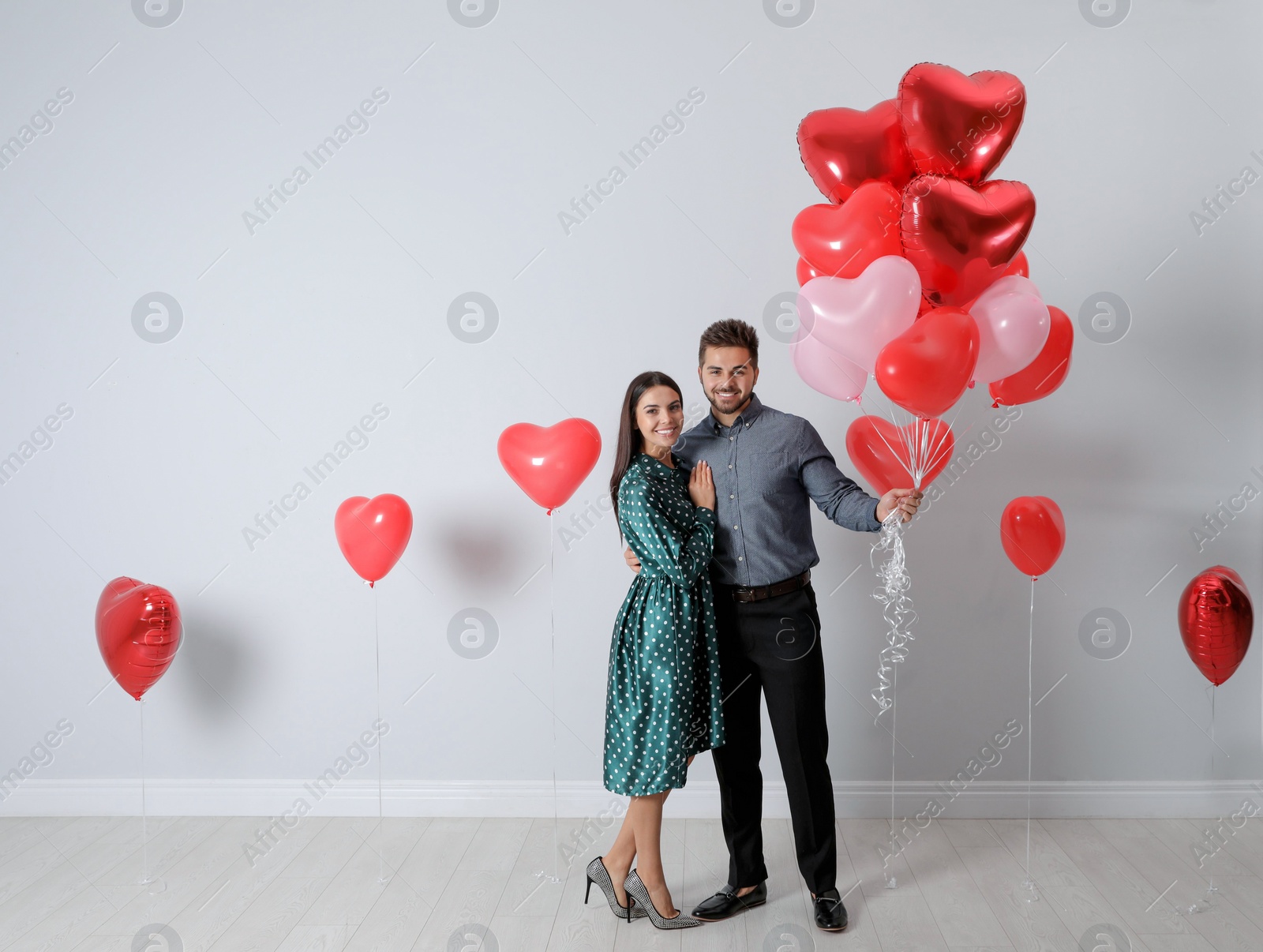 Photo of Happy young couple with heart shaped balloons near light wall. Valentine's day celebration