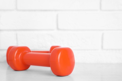 Stylish dumbbells on table against brick wall, space for text. Home fitness