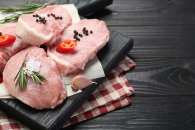 Photo of Pieces of raw pork meat with chili pepper and spices on black wooden table. Space for text