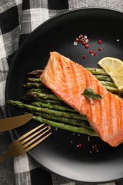Photo of Tasty grilled salmon with asparagus, lemon and spices served on table, top view