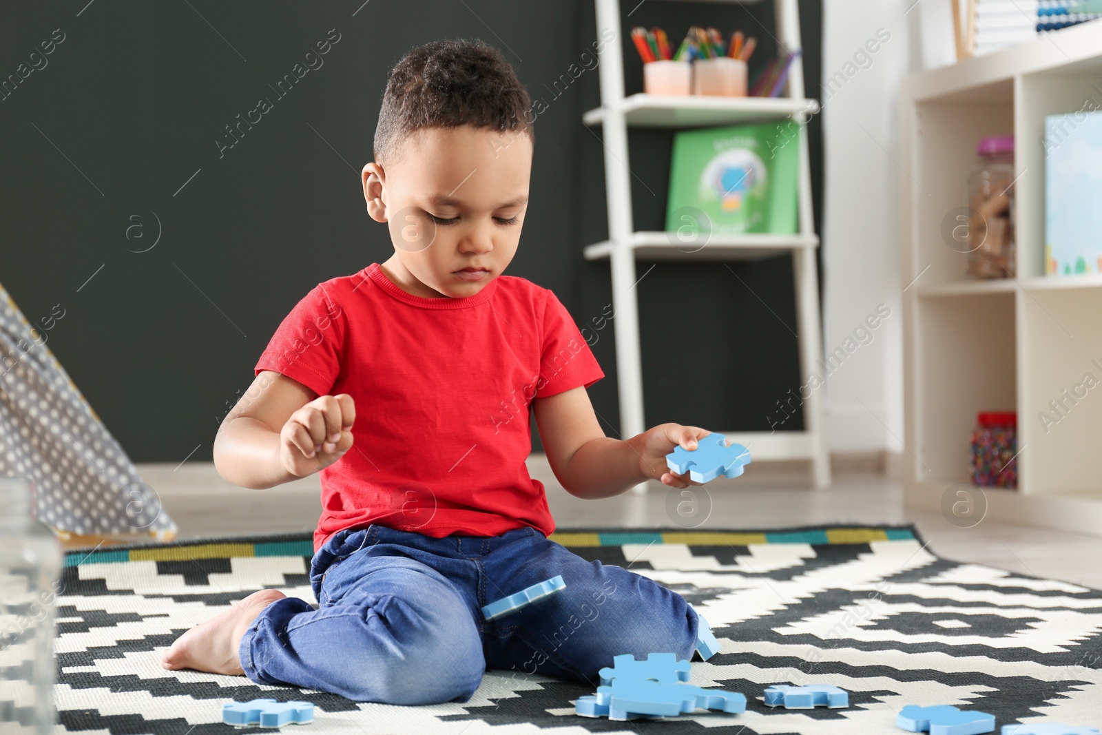 Photo of Cute little African-American child playing with puzzles on floor in kindergarten. Indoor activity