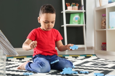 Cute little African-American child playing with puzzles on floor in kindergarten. Indoor activity