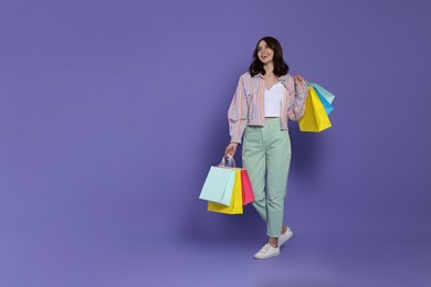 Photo of Beautiful young woman with paper shopping bags on purple background