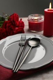 Photo of Romantic place setting with red roses and candles on wooden table, closeup. St. Valentine's day dinner