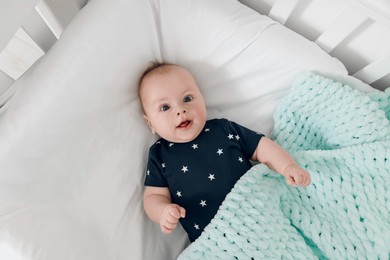 Photo of Cute baby under soft plaid in bed, top view