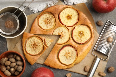 Photo of Nutmeg powder, seeds, tasty apple pie and fresh fruits on grey table, flat lay
