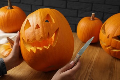 Photo of Woman with carved pumpkins and knife at wooden table, closeup. Halloween celebration