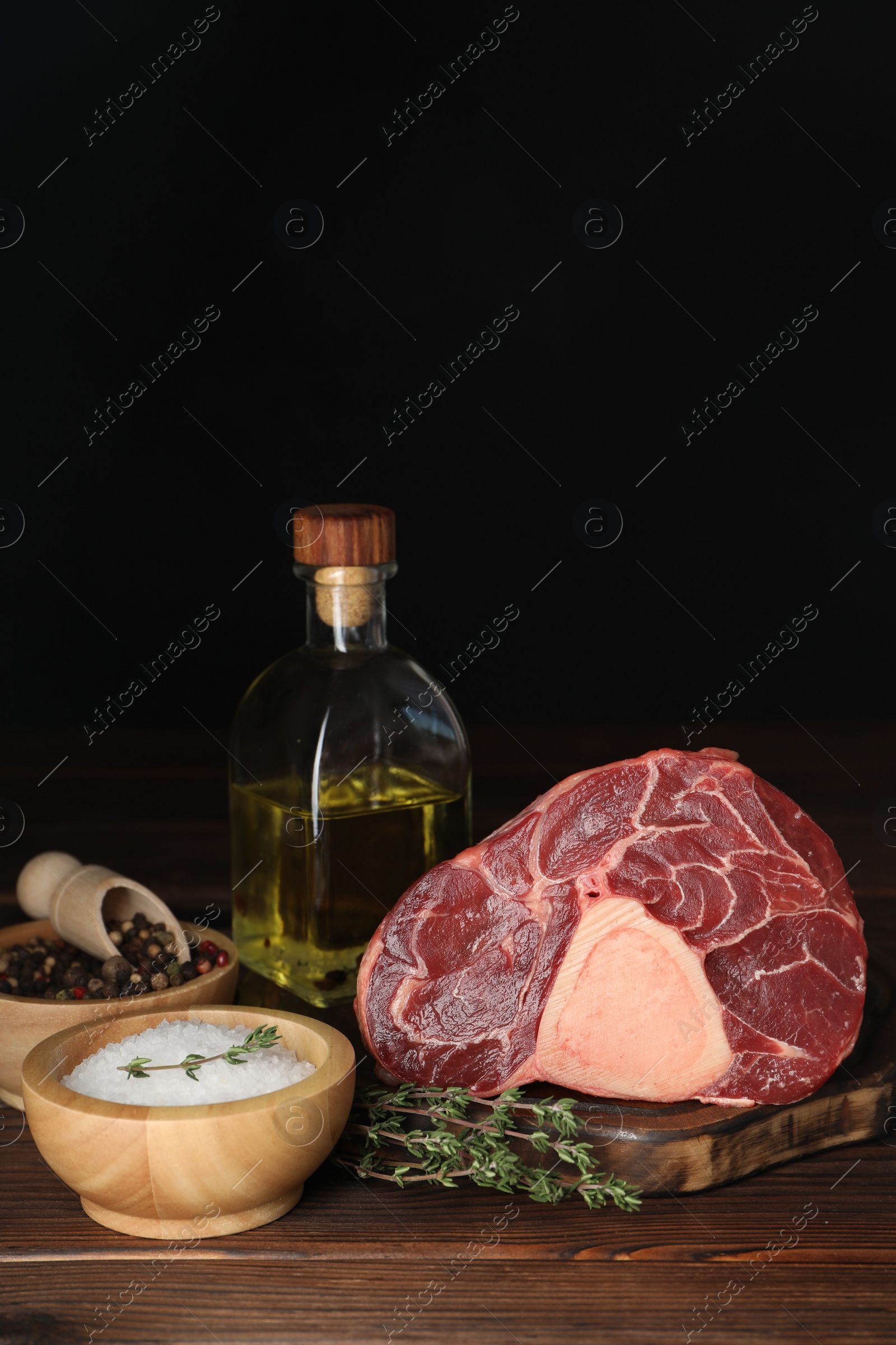 Photo of Piece of raw beef meat, thyme, oil and spices on wooden table against black background